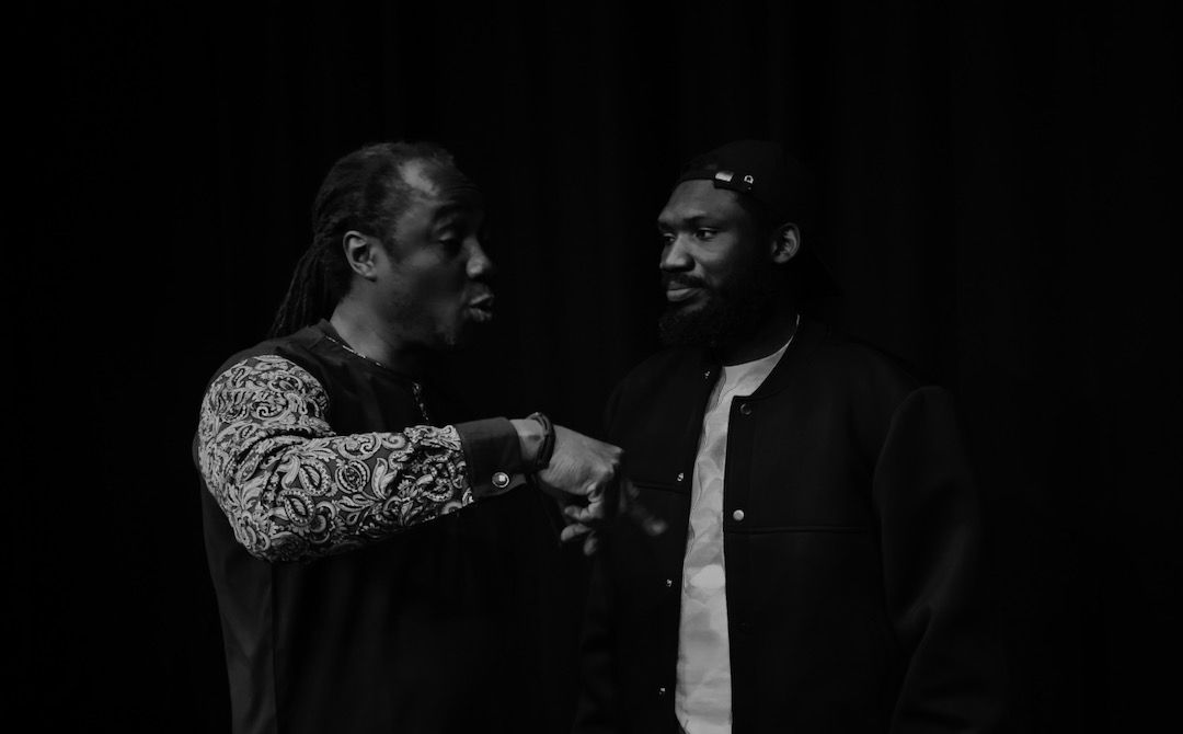Two performers in conversation on stage, black and white