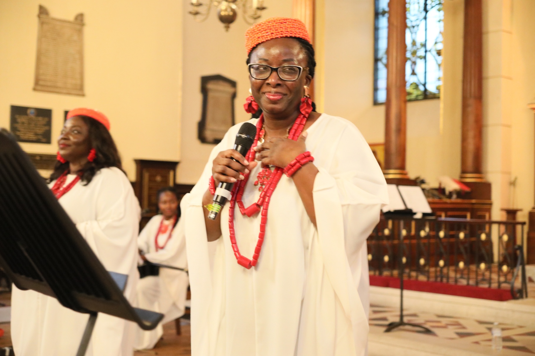 Performer in coral regalia holding a microphone